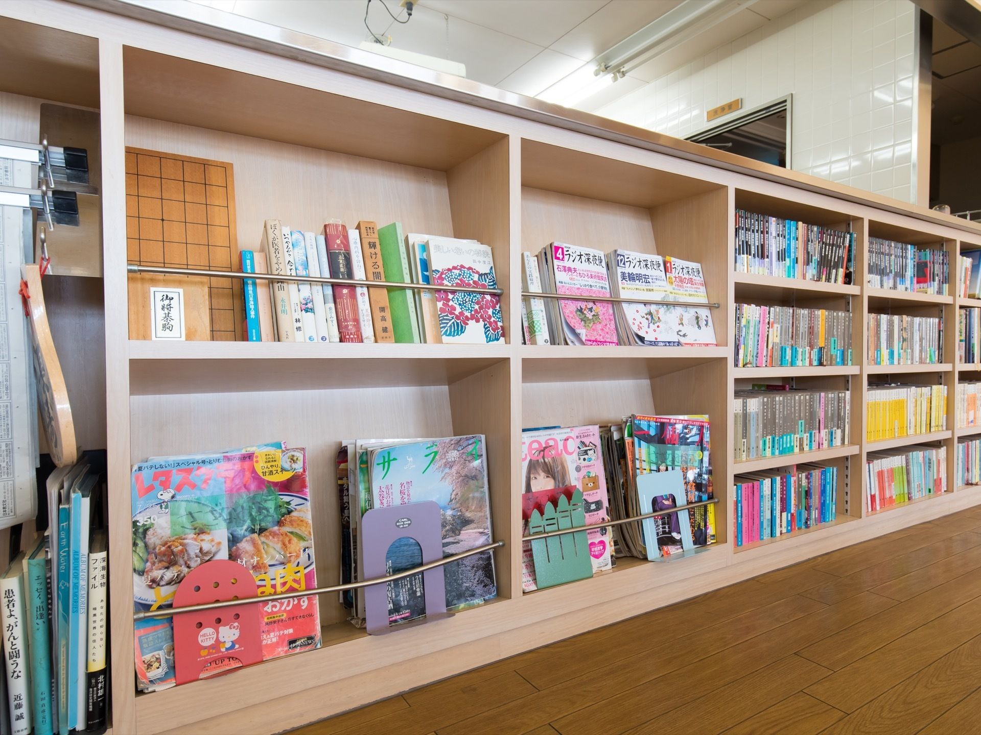 共有スペースの背の低い棚にはさまざまな種類の本や雑誌、新聞が収納されていて、自由に手に取れるようになっている。