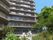 12階建ての大きな建物はグレー系で各フロアにベランダが付き、周辺には花も植えられている。