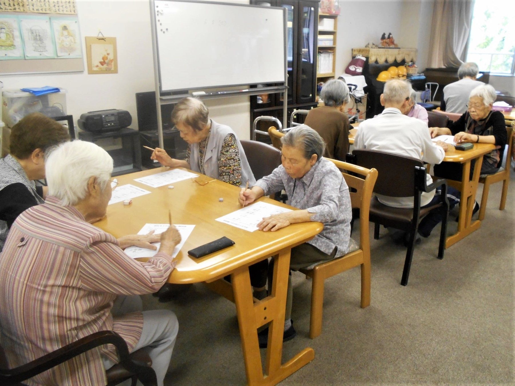 入居者が３つのテーブルに座り、それぞれプリントに取り組んでいる様子。