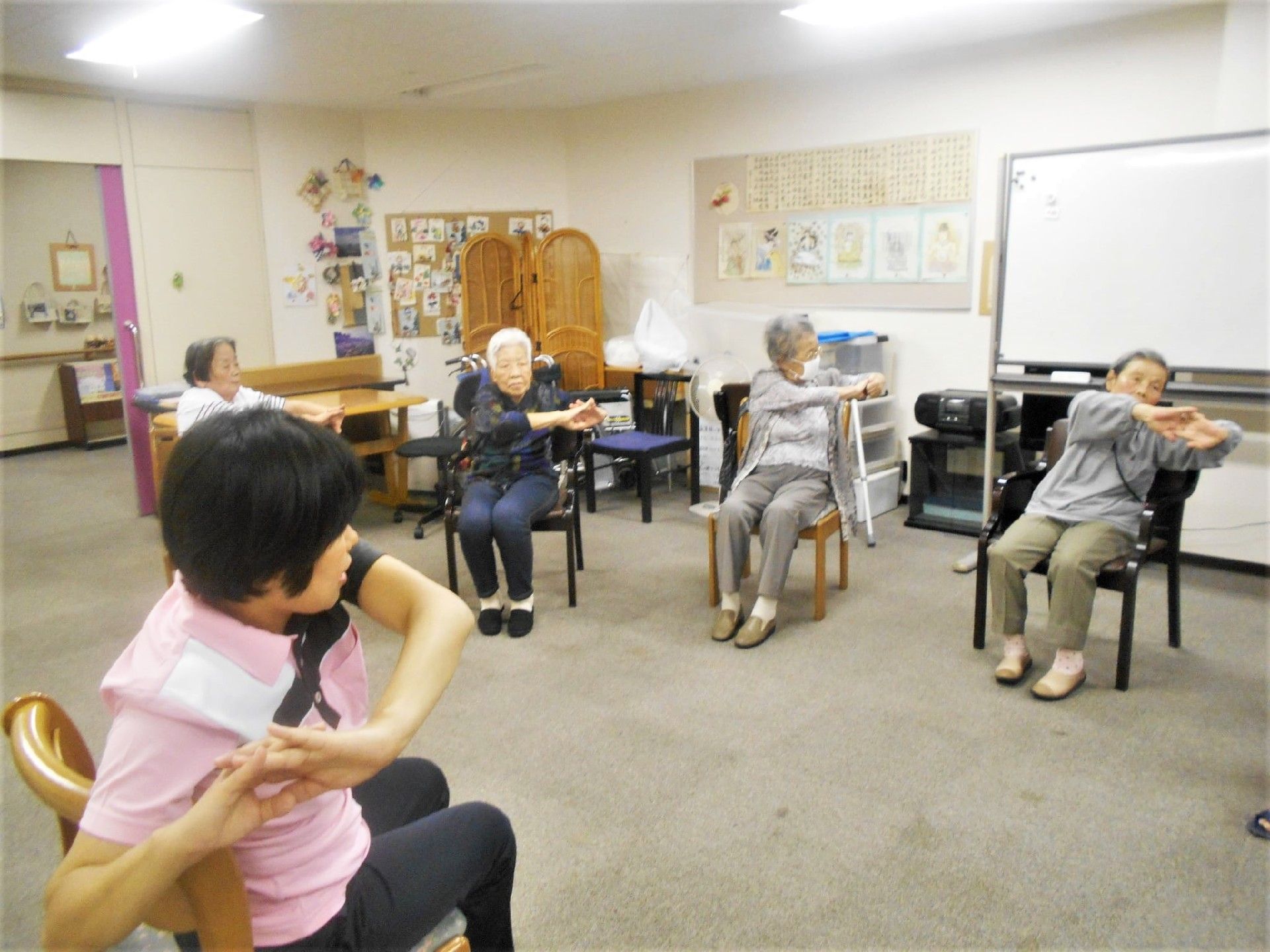 椅子に座ったスタッフを中心に両手を組んでストレッチをしている様子。