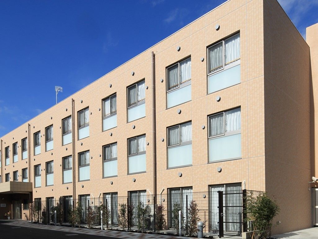 薄茶色の３階建ての建物には、同じデザインの窓が規則的に並んでいる。建物の前にはタイルで、通路を整備したデザインを採用している。