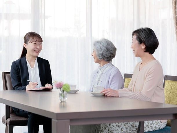 ひざ掛けをして車椅子に乗る男性と、横にひざまずいて話を聞く男性スタッフ