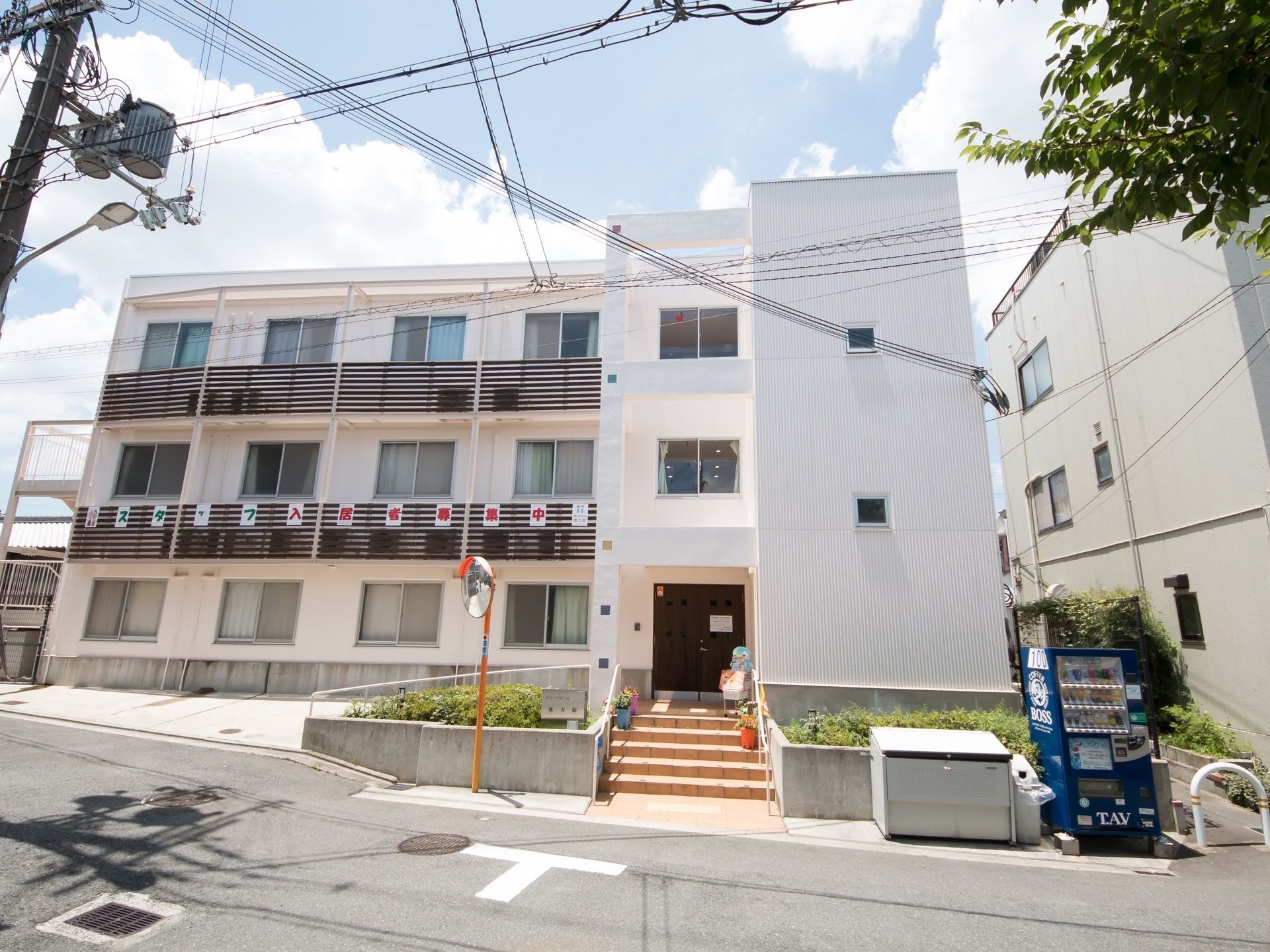 ３階建ての綺麗な外観。駐車スペースが２台分あり、すぐ横にスロープがある。スロープを上るとすぐに玄関の扉がある。