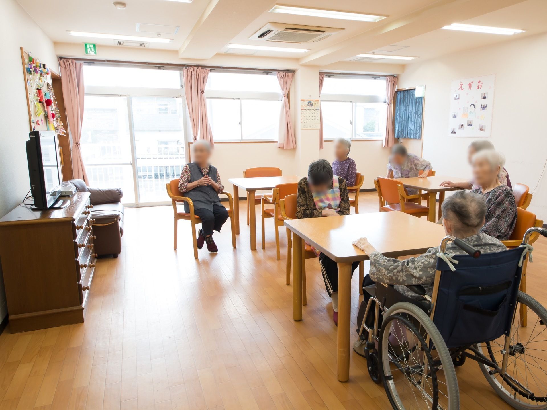 椅子やテーブルが置かれており、入居者様が席についている。窓がたくさんある明るい空間になっており、天井には空調も設備されている。