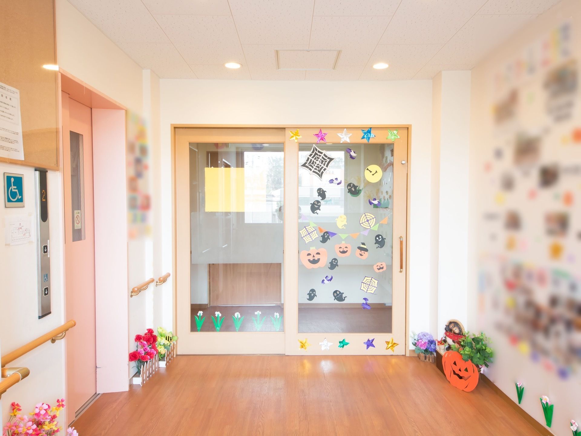通路に入居者様が制作した花、季節の作品などが飾られている。備えつけの扉にも、色鮮やかな作品が貼られポップな雰囲気である。