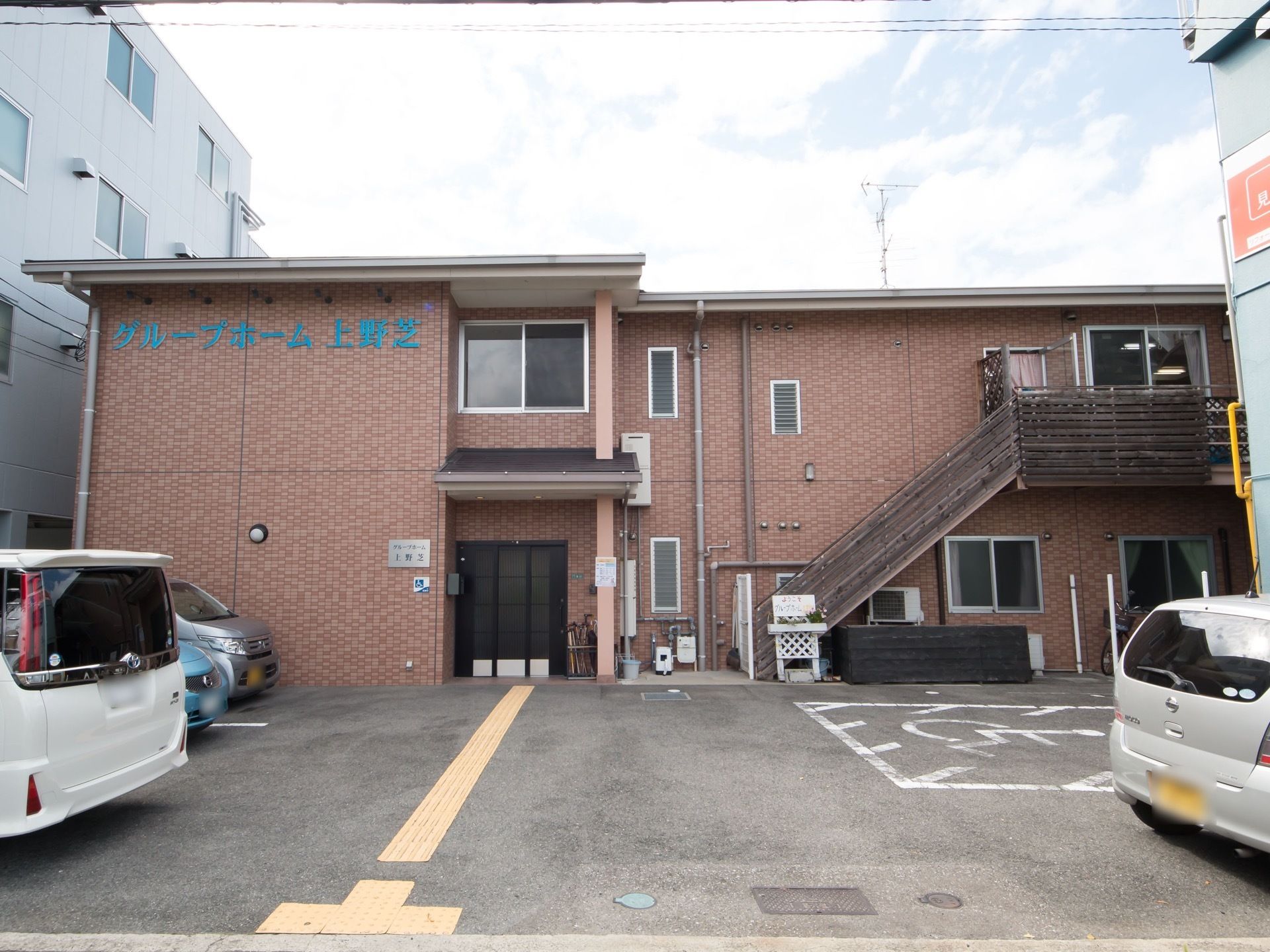 ２階建ての建物である。茶色の壁には施設名が青色で書かれている。駐車場内に点字ブロックが設置されている。