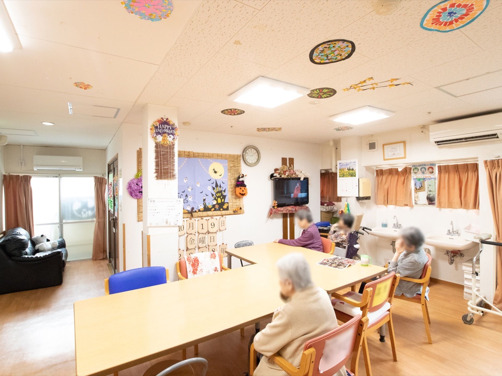 左奥に黒色のソファが置かれている。右側の壁に洗面台が設置されている。中央には２つのダイニングテーブルが配置されている。