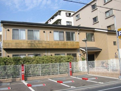 コインパーキングと、植栽に囲まれたベランダつき二階建ての建物