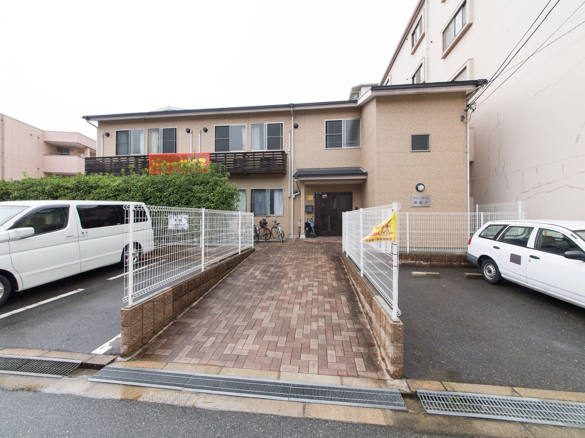道路から玄関までは、長いレンガ張りの通路が伸びている。二階建ての建物で、二階部分にはベランダが付いている。