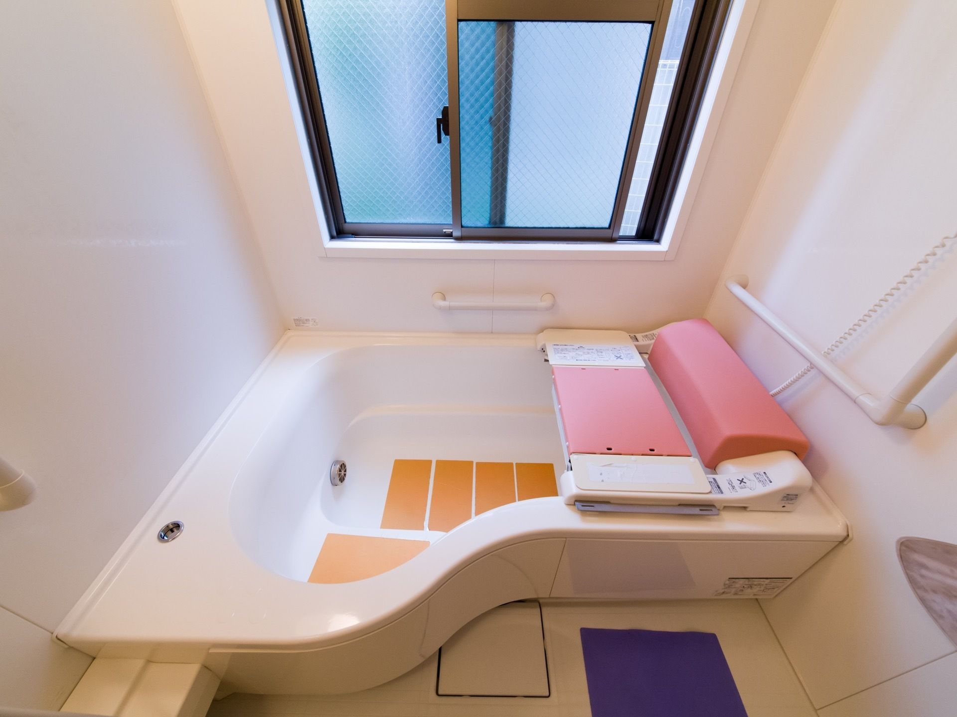 長方形の窓がある。浴槽にはすべり止めが付いており、入浴を補助する器具が設置されている。手すりがある。