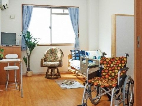 ベッド、テレビ、椅子、テーブル、車椅子が置かれている部屋