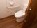 居室に設置された個人用のトイレ内部。淡い花柄の壁紙が貼られた壁にはL字の手すりとナースコールが付いている。