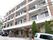 白と茶色でまとめられた4階建ての外観である。手前の道路は少し坂道になっていて、道路わきに2台の車が置いてある。
