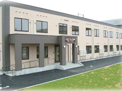 「シルバーピュア一関」の外観。田んぼや畑、少民家など静かで住み心地の良い、木造2階建てのこげ茶色と白色の外観。