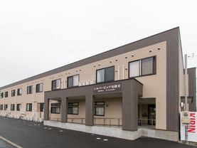 玄関ポーチの前にスロープが付いている。スロープには手すりが付いており、屋根がある。スロープ上の屋根に施設名が付いている。