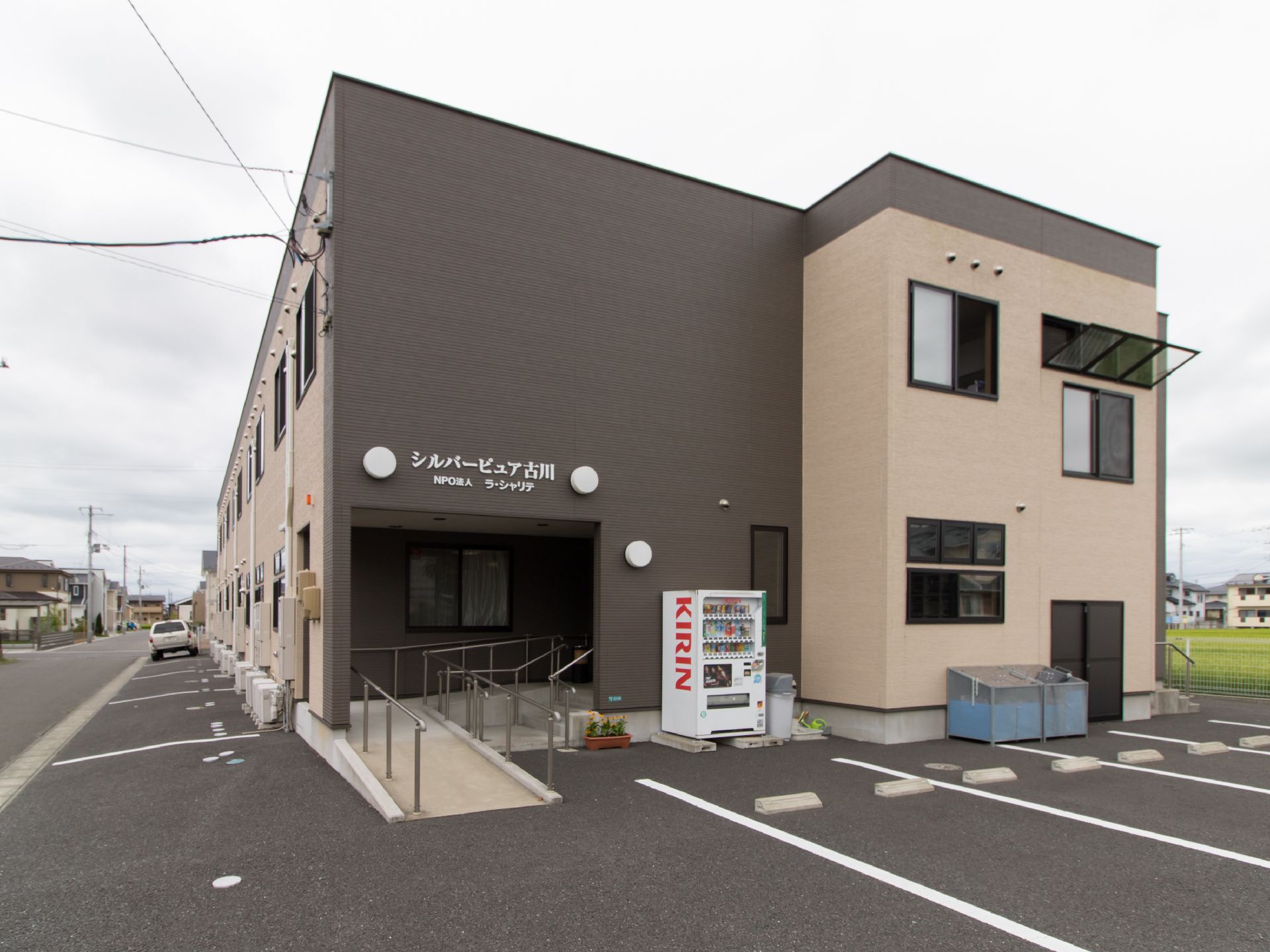ベージュとブラウンのツートンカラーの建物である。駐車場が設けられている。施設名が正面玄関に掲げてある。