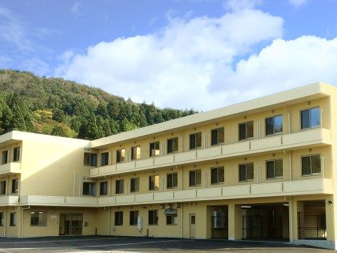 周囲に森が広がる場所に立地する、クリーム色の三階建ての建物