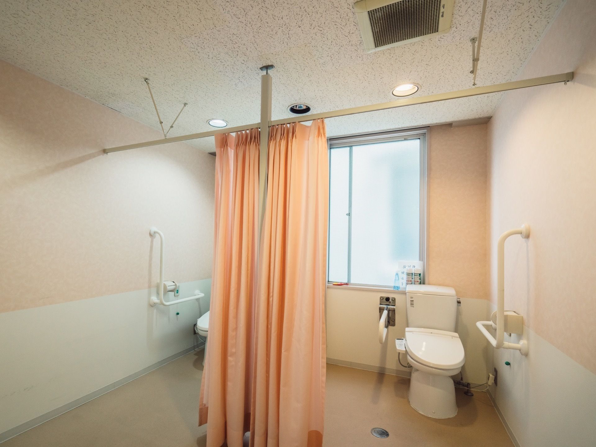 便座が、間隔を空けて２つ並んで設置されている共用トイレがある。それぞれカーテンで目隠しできるようになっている。