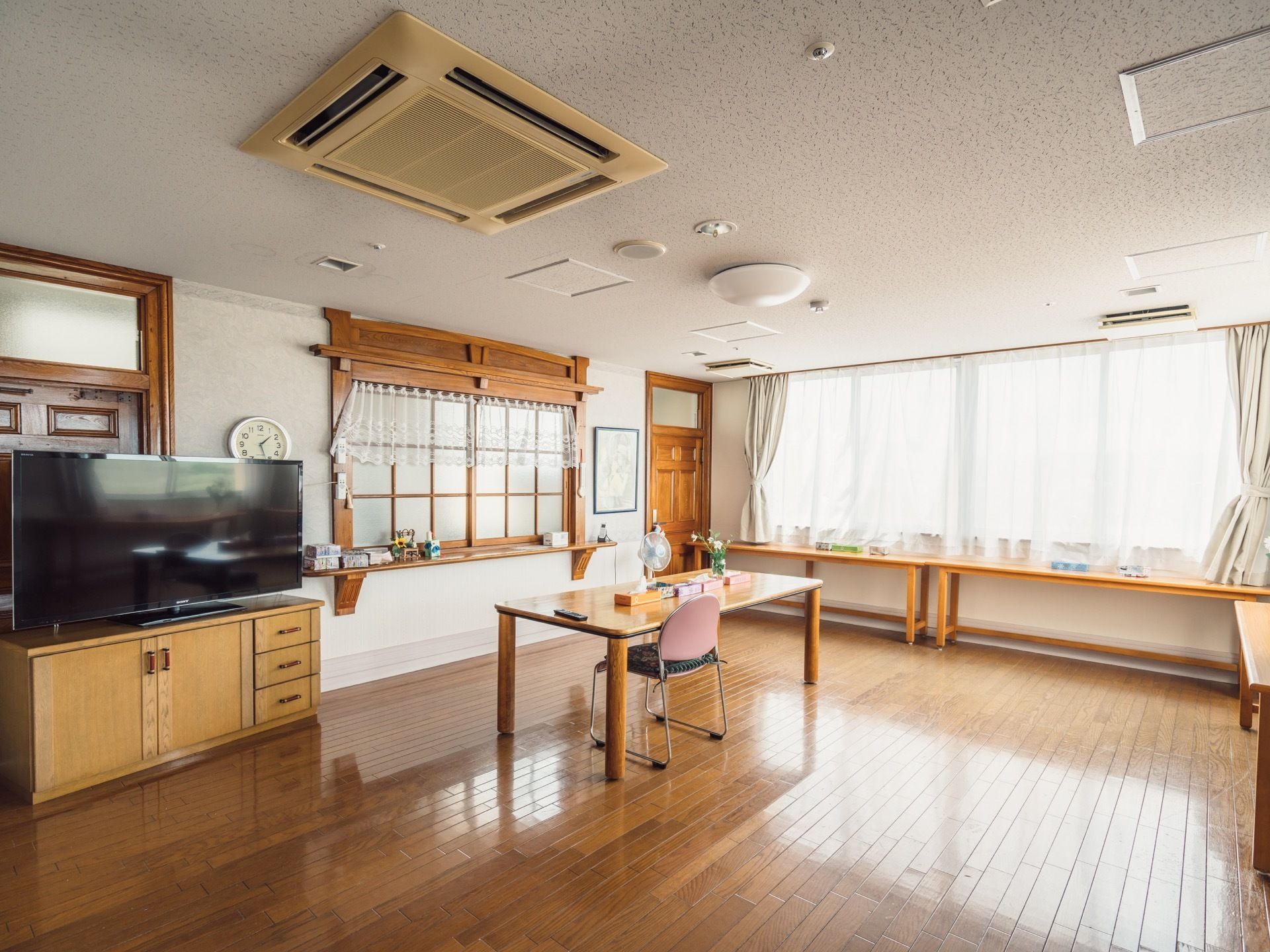 壁一面に窓があって、とても明るい空間が休憩スペースになっている。テーブルに椅子が１脚置かれている。大画面テレビがある。
