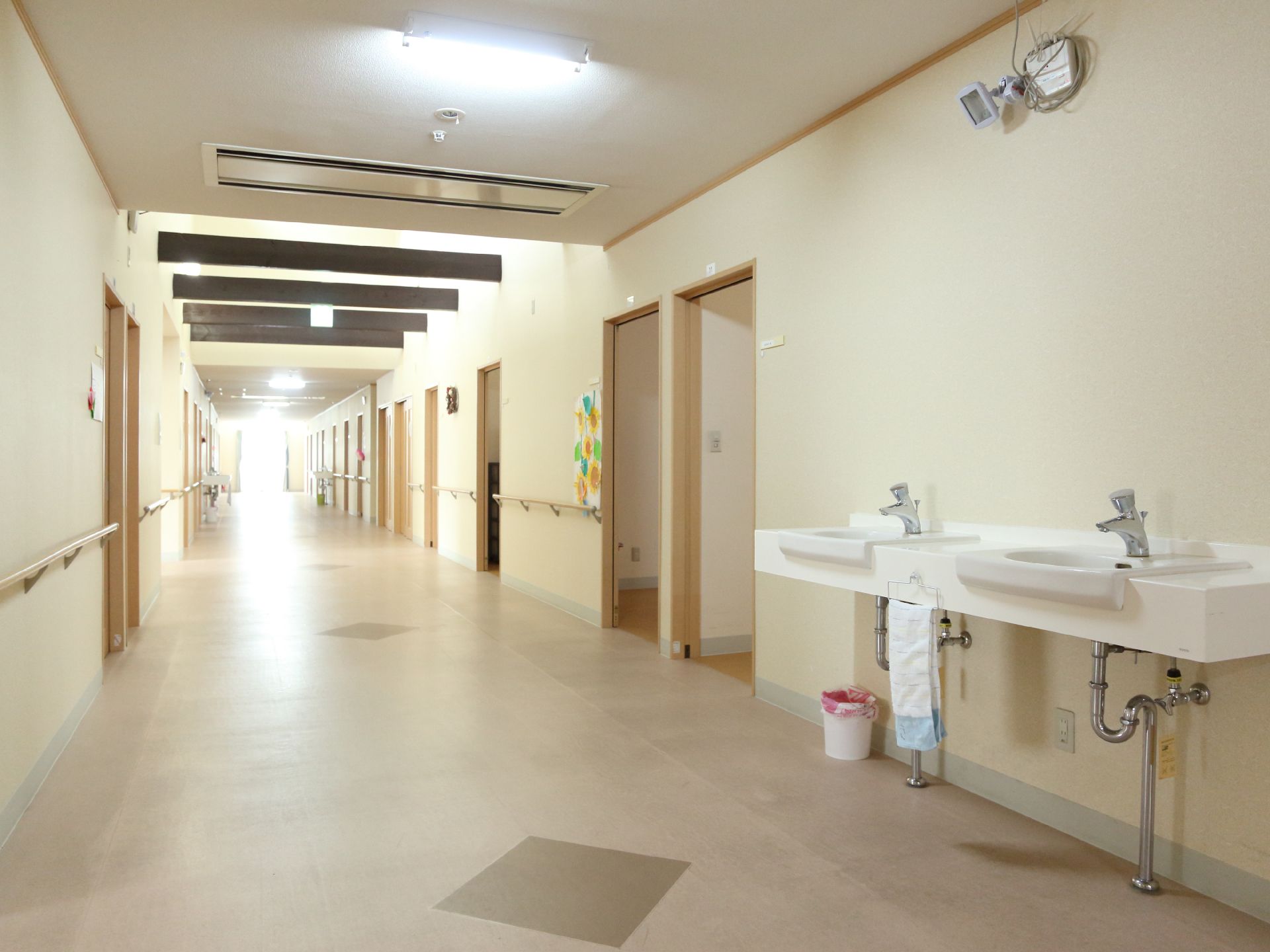 長く続いている廊下には左右に居室が並んでいる。壁には手すりが付いていて、洗面台が2つある。洗面台の下にくず入れがある。