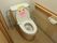 蓋の内側にピンクのウサギが貼ってある。左手には手すりとトイレットペーパーが取り付けられている。レバーを回して水が流れるタイプのトイレである。