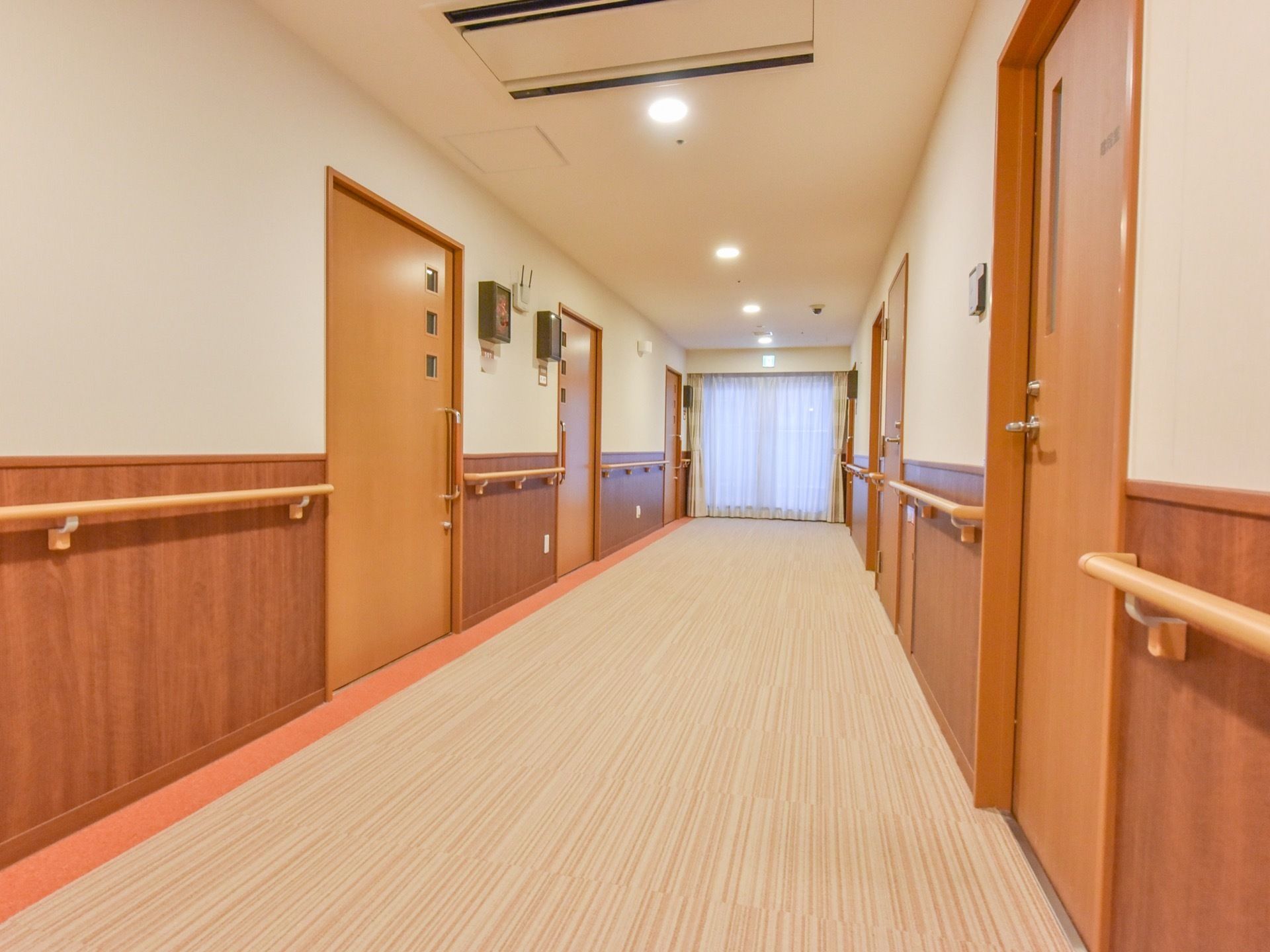 白と茶色のツートンカラーになっている通路の壁には、長い手すりが隙間なく設置されている。円形のライトが天井に並んで付いている。