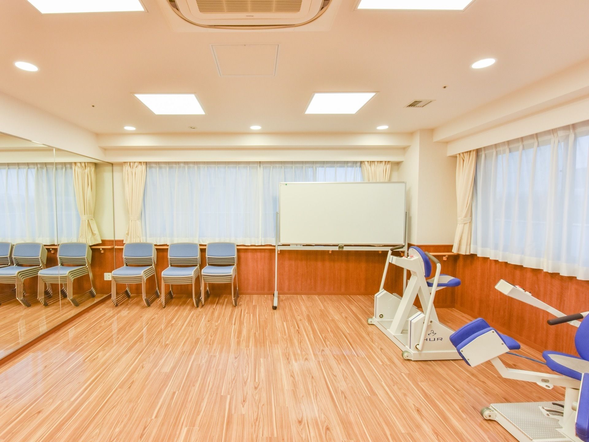 正面の窓際にはホワイトボードがあり、その左横には数多くのイスが積み重ねて置いてある。すぐ横の壁は鏡になっている。