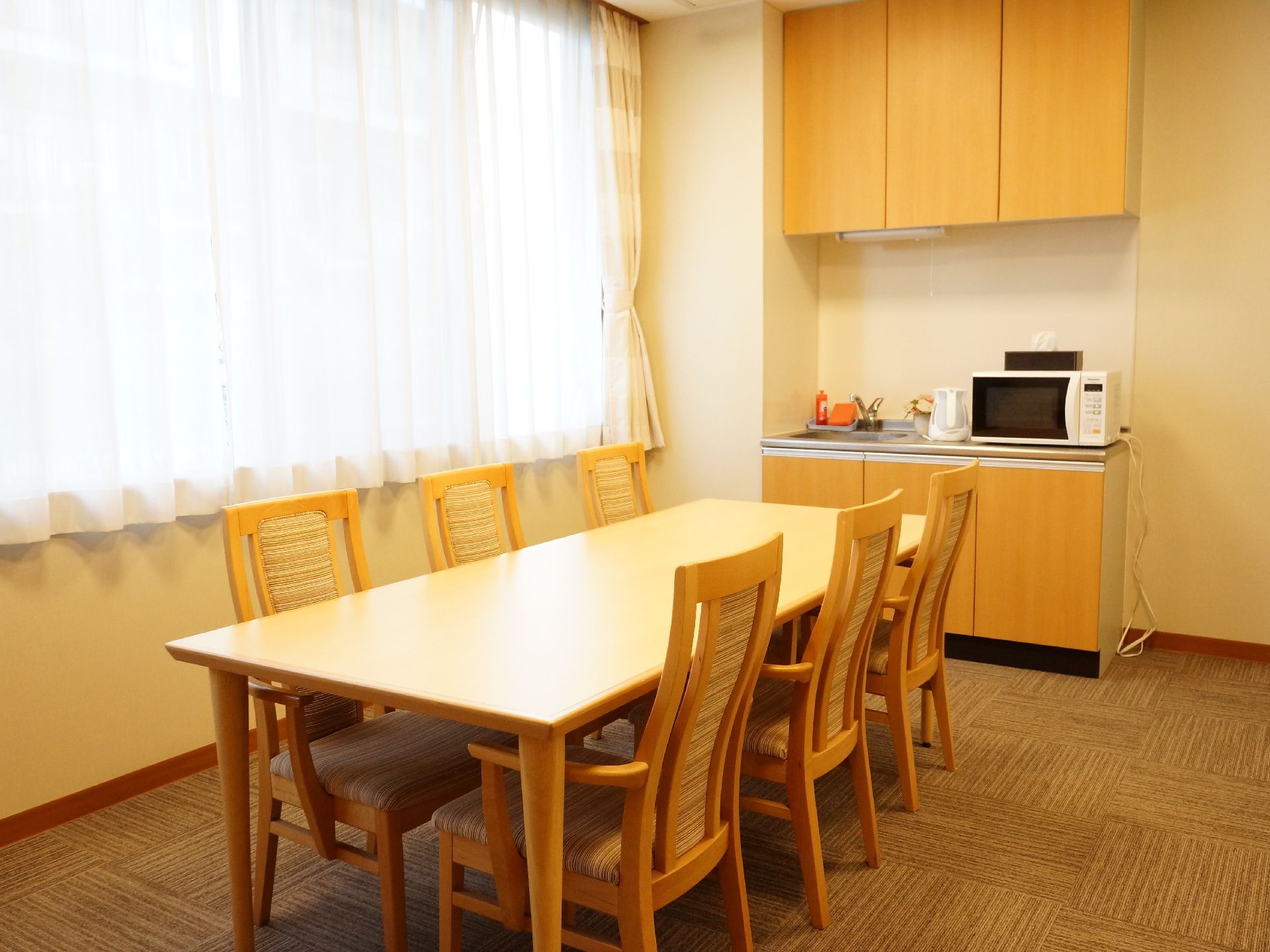 部屋の端に長しとレンジが置ける大きさのミニキッチンがある。上にも棚がある。6人掛けのダイニングテーブルセットが置いてある。