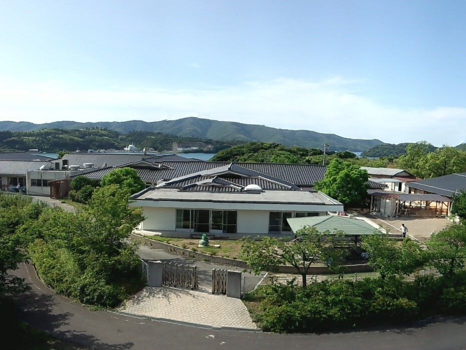 平屋建ての和風の住まい。周辺には緑の木が多く植えられ、敷地内には庭があるのも見える。