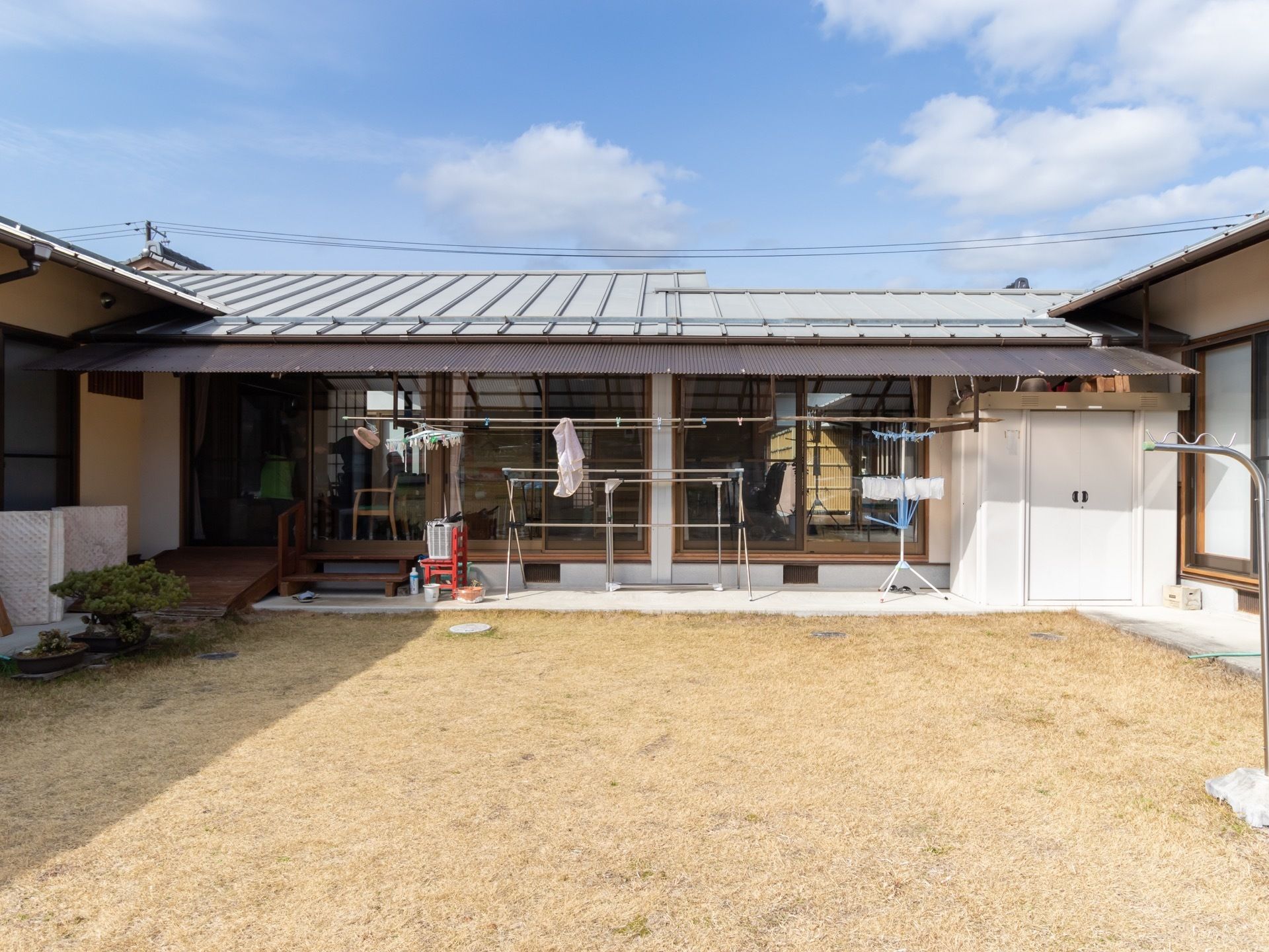 ひさしの下に物干しがある。右手には白い物置、左手にはスロープ。また、スロープの先には盆栽が置かれている。