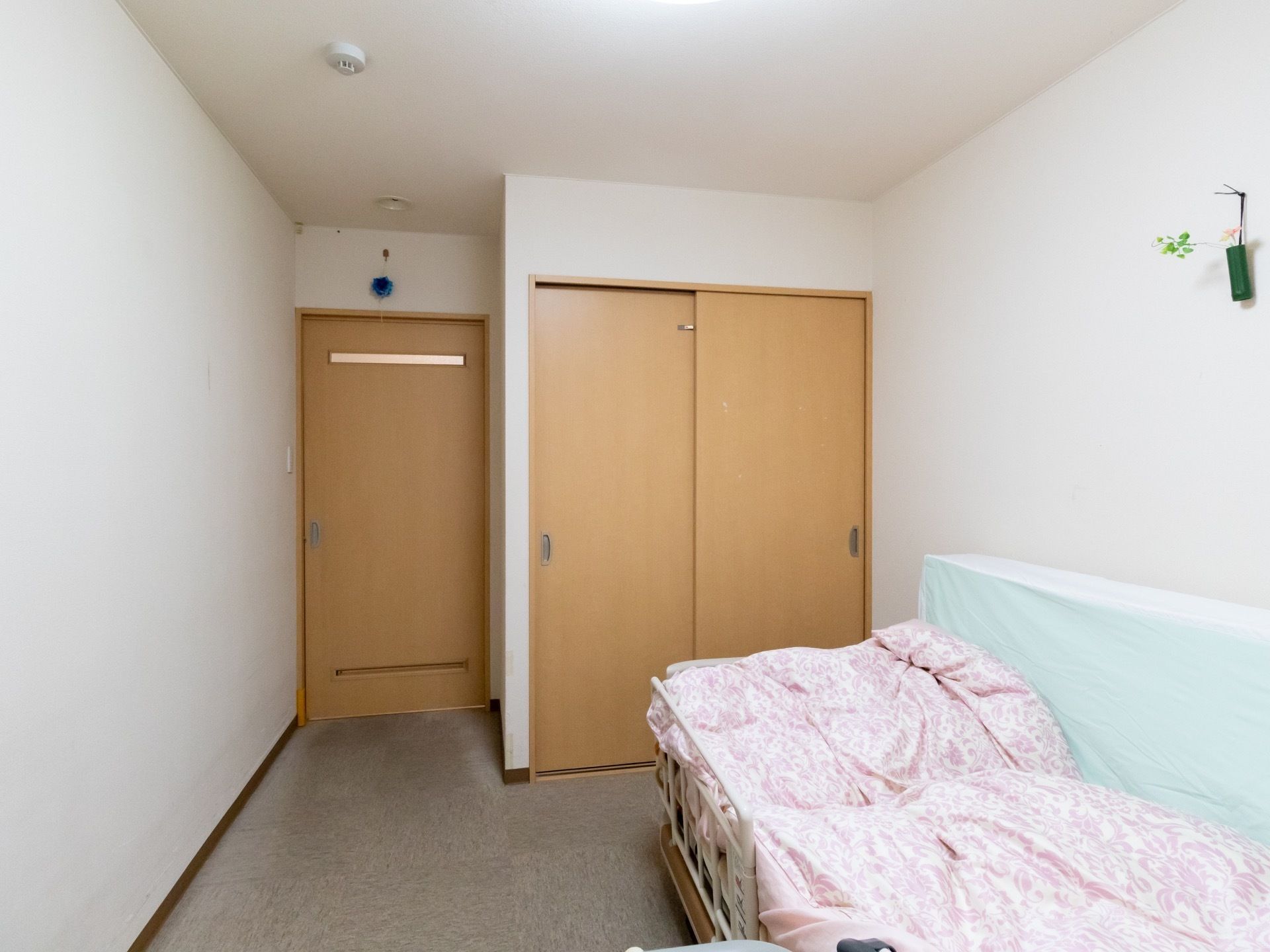 白い壁の居室である。入口の扉はスライド式となっており、壁際にベッドが１台置かれている。また、壁には飾りが飾ってある。