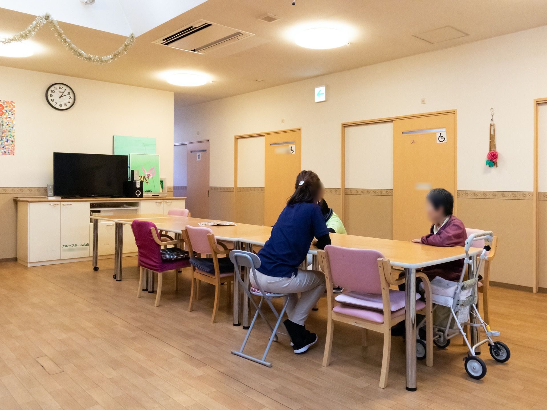 横長の大きなテーブルが中央に置かれており、その周りに、スタッフと入居者様が座って話をしている様子である。