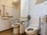 洗浄機能付きの便座が２個並んだトイレである。間仕切りには、白いカーテンが下がっている。それぞれ、便座の両脇に手すりが取り付けてある。
