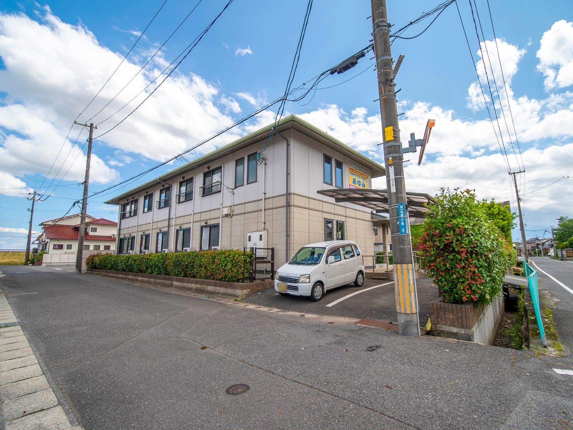 ベージュとアイボリーの外壁が特徴的な２階建てのホームである。建物の周囲には、生垣が設けられ整備されている。