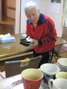 手前に沢山のコップが並んでおり、高齢者が運ぼうとしている。