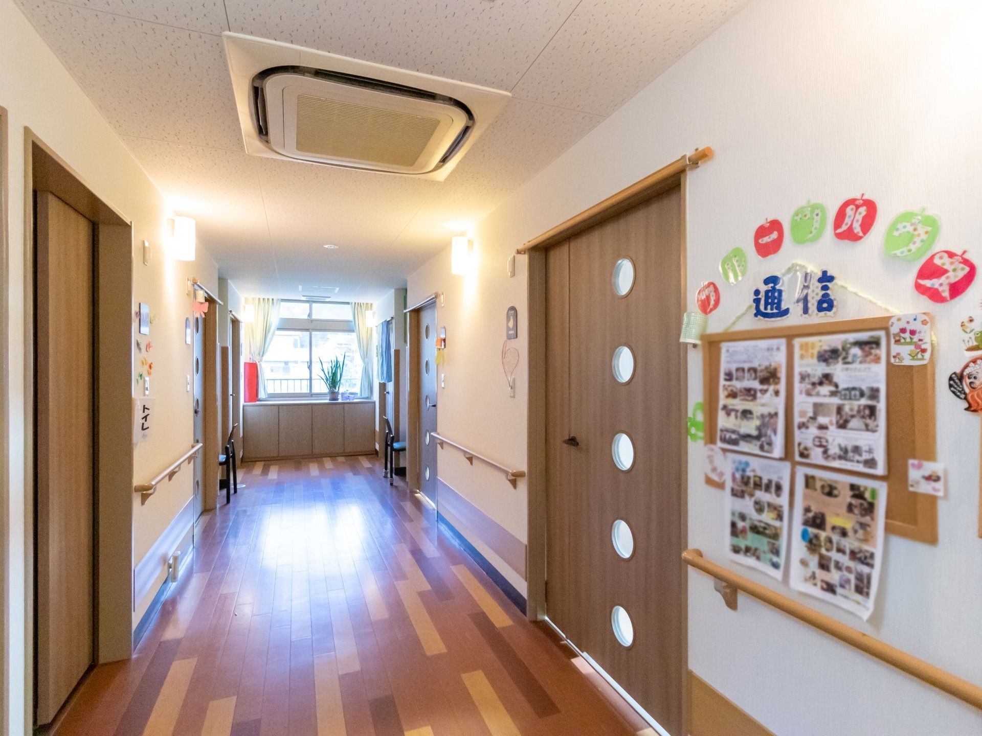 幅広の通路があり、左右の壁に、丸い小さなガラス窓が取り付けられた木目の扉が並んでいる。扉と扉の間には黄土色の手すりも設置されている。