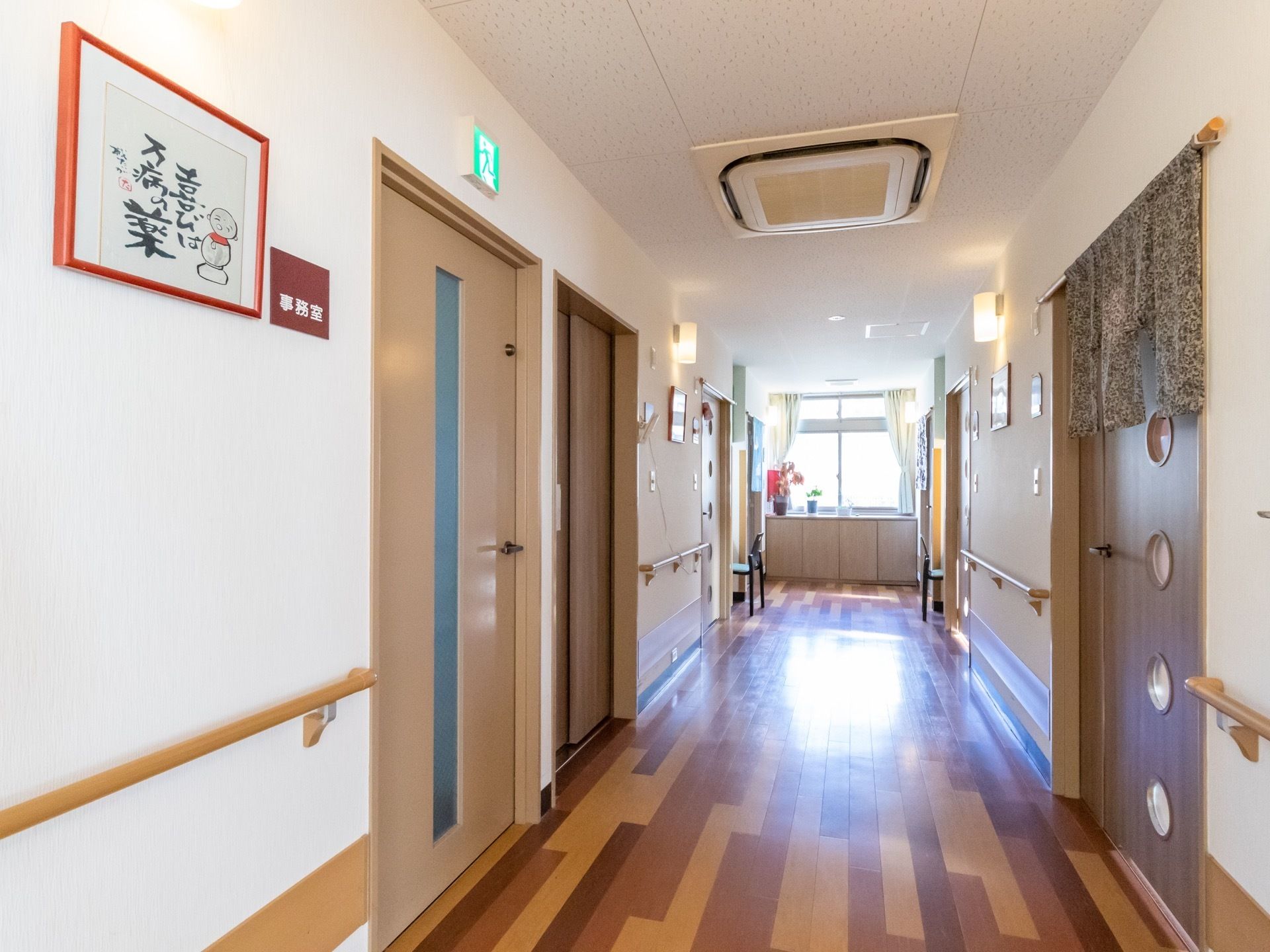 館内の通路にたくさんの扉が並んでおり、その内の１つの扉の横に、事務室と書かれた四角のプレートが貼られている。