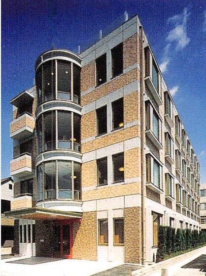 レンガ調の外壁の４階建ての建物の玄関には屋根が付き、側面には一面ガラス張りとなっているサンルームのような場所がある。