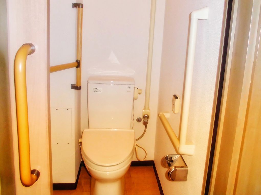 手すりがたくさん付いたトイレ。便座はシンプルなデザインでトイレットペーパーホルダーも設置されている。