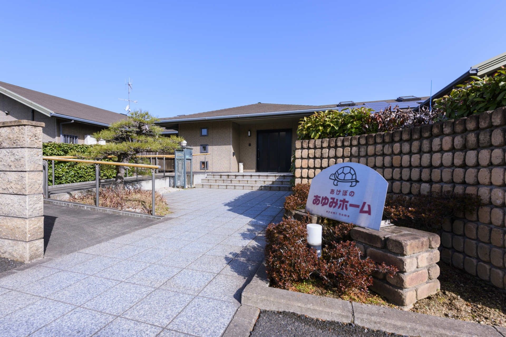 水の入ったコップを持って微笑んでいるエプロンを付けた女性スタッフと薬を飲もうとしている高齢女性。