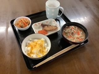 グレーの大きなリュックサックを持って笑顔で座っている高齢男性の手にはビンゴの紙が握られている。