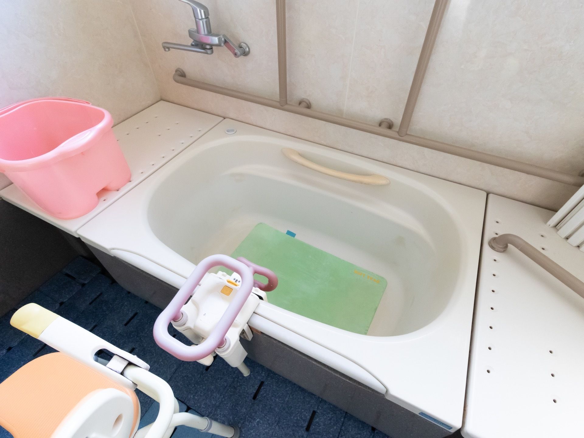手すりやバスボードの備え付けられている浴槽があり、浴槽の横にはシャワーチェアや足湯バケツが置かれている。