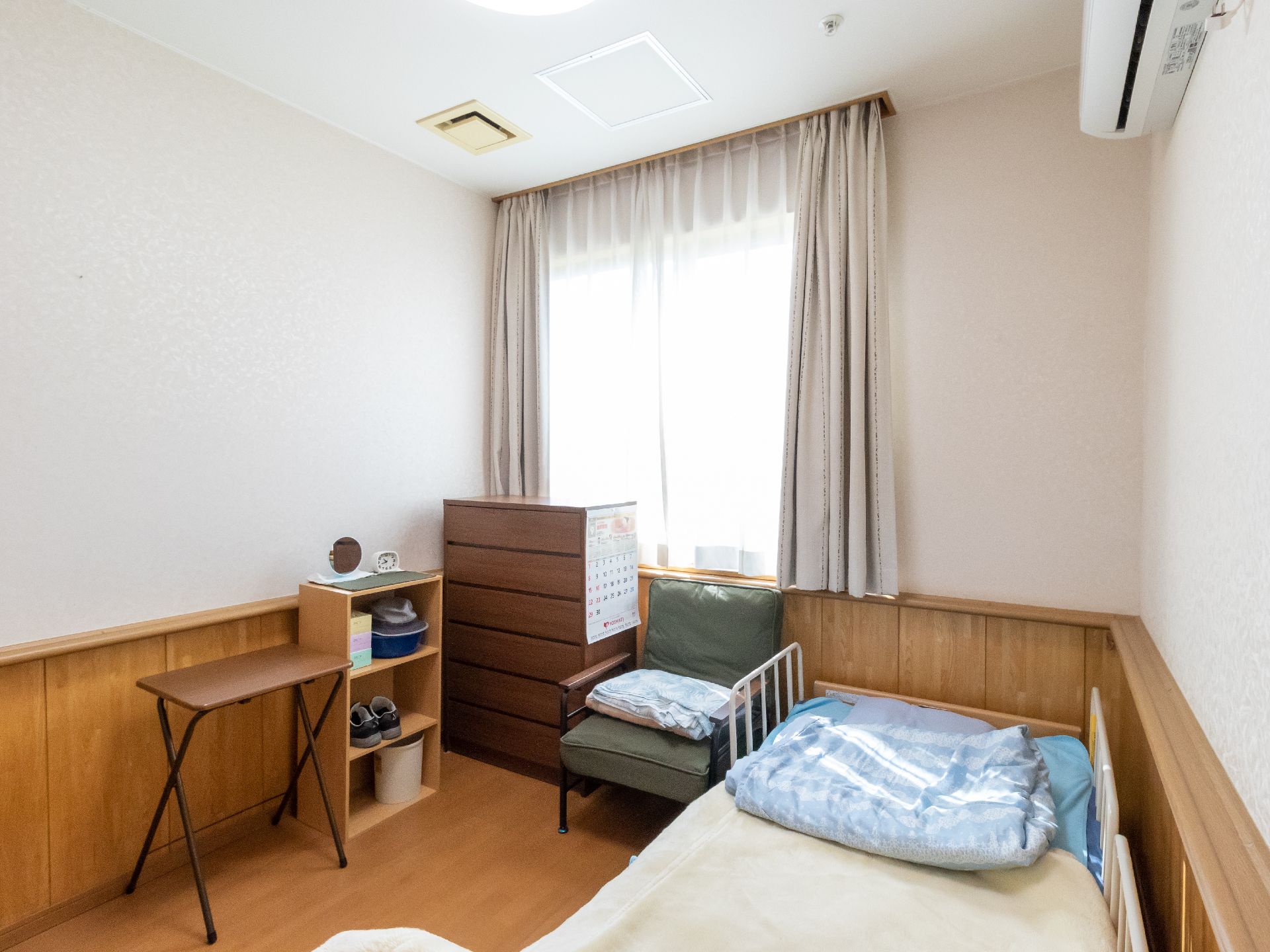 ベッドとタンス、椅子や棚が置かれた部屋全体に手すりがついている居室