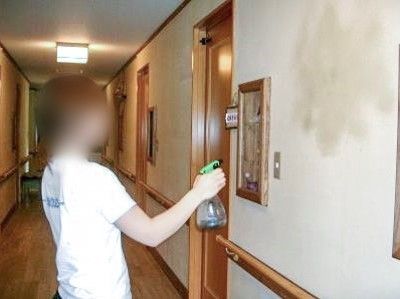 廊下は、白壁と柔らかい木材を使用した体に優しい作りの内装となっている。女性スタッフが壁に霧吹きをかけている。