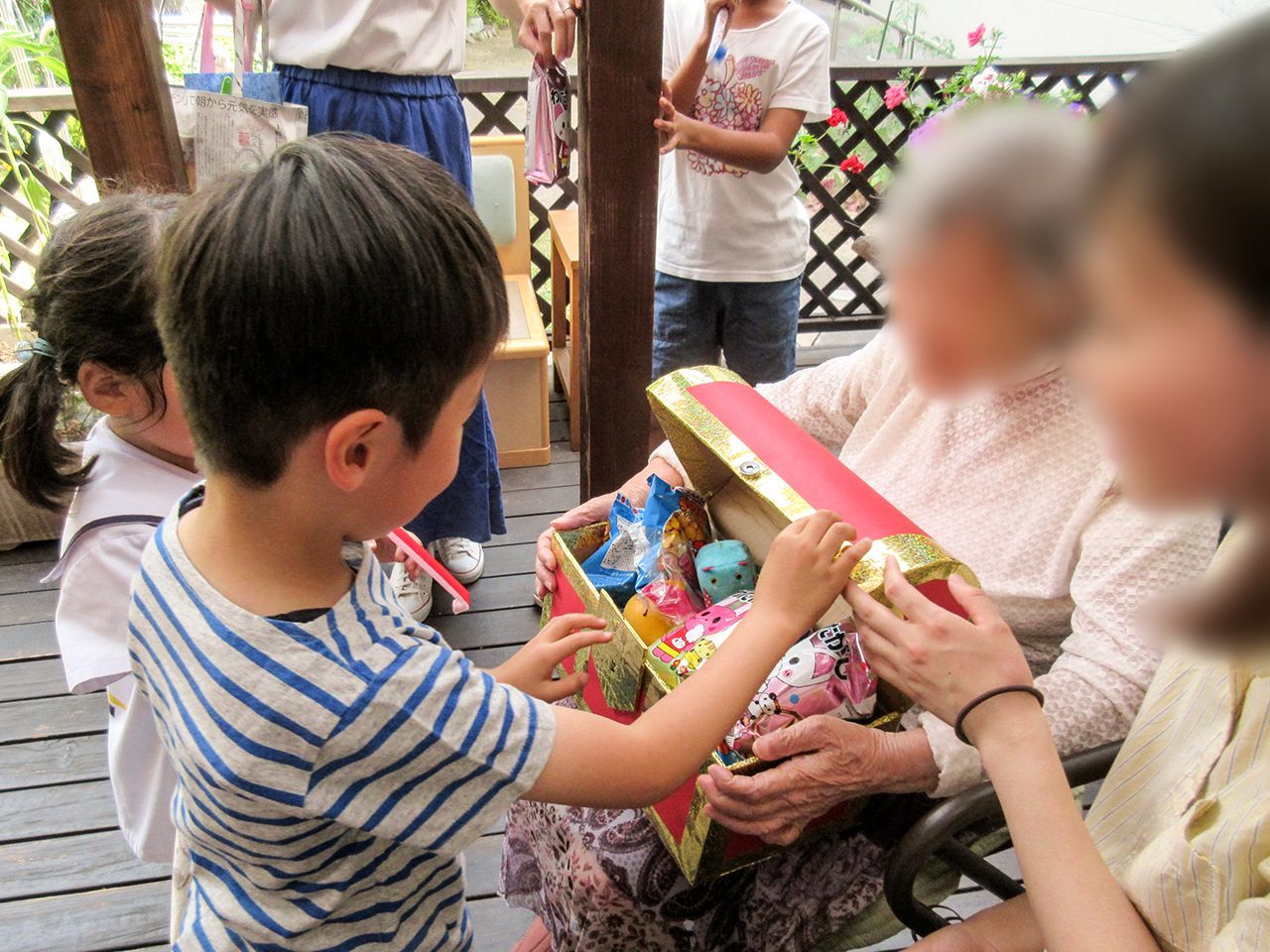 施設のウッドデッキで開催されたイベントでは、入居者様がお菓子を持って小さな子どもたちと交流を深めている。