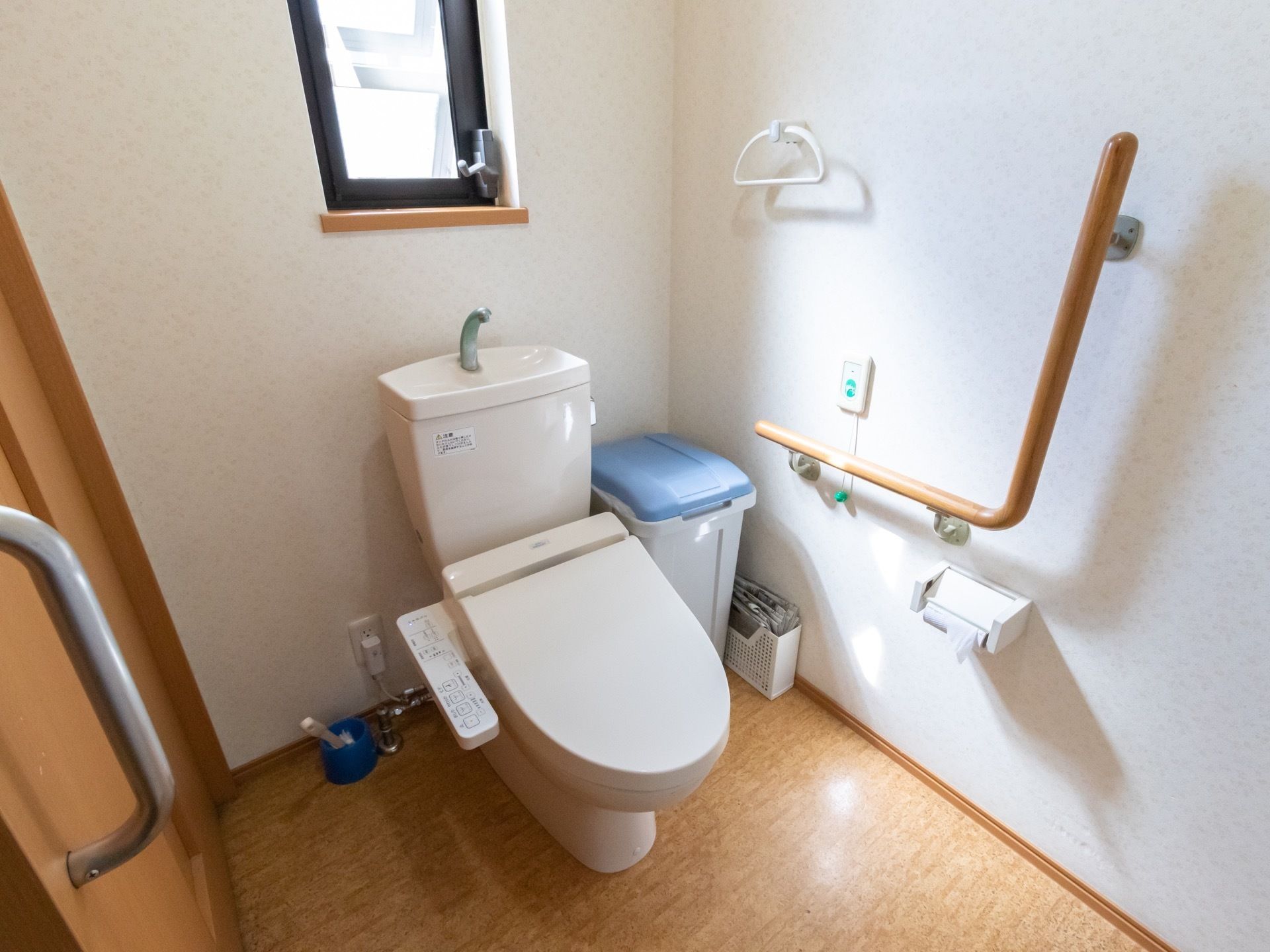 トイレは明るく清潔感があり、広めのスペースになっている。壁にはL型の手すりや呼び出しボタン、タオル掛などがかかっている。