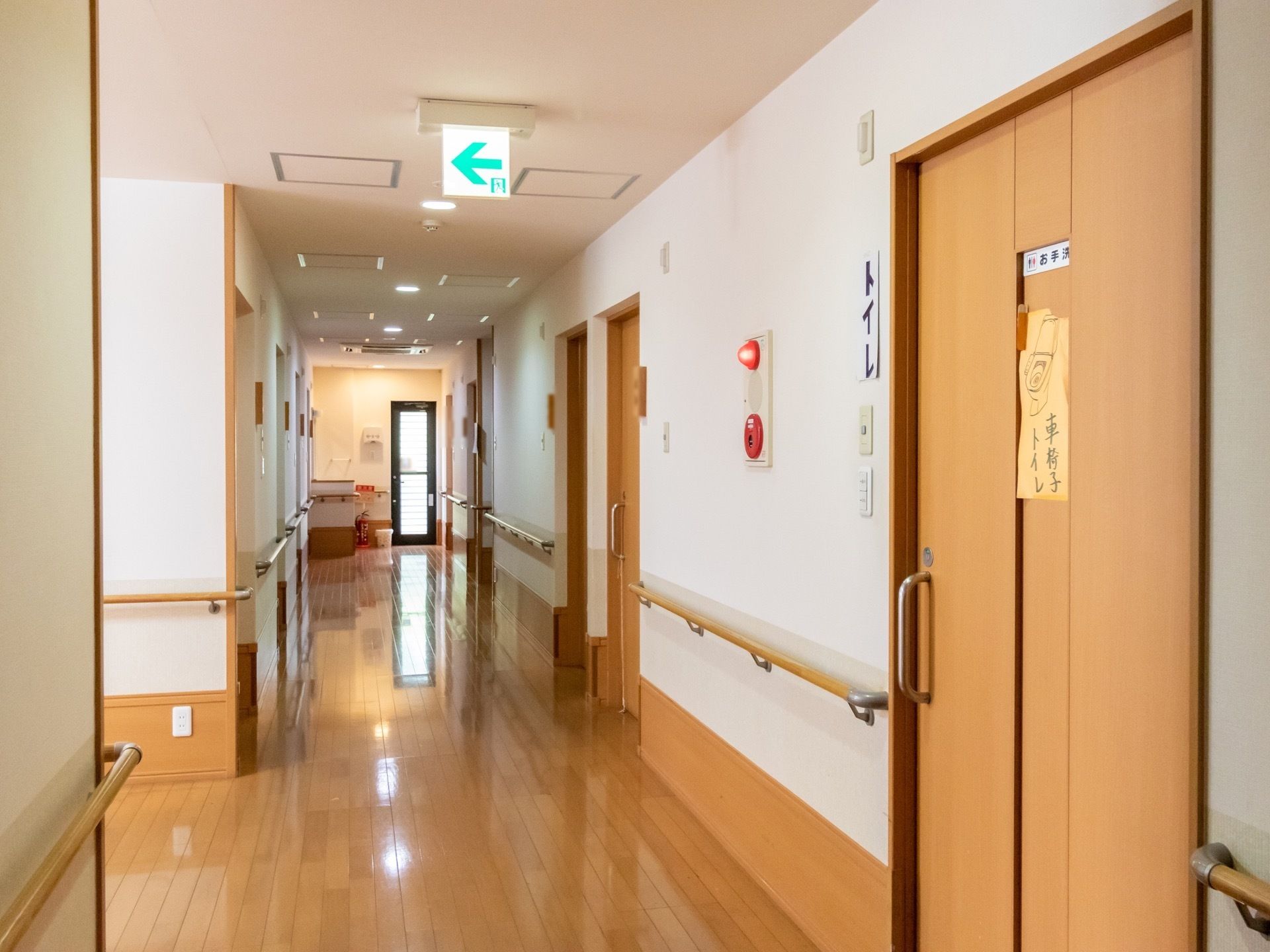通路の床はフローリングになっており、引き戸式のドアが並んでいる。壁には手すりや、火災報知器がある。