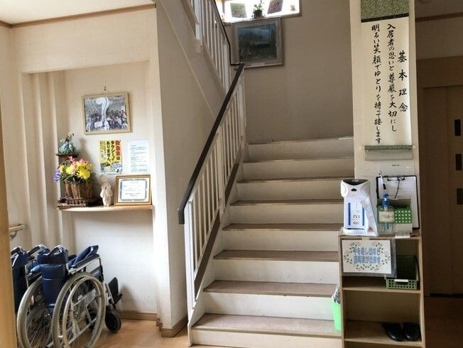 ホールは広く折りたたまれた車いすが置かれ、目の前にある階段には手すりが付き、理念が筆で書かれた掛け軸のようなものが飾られている。