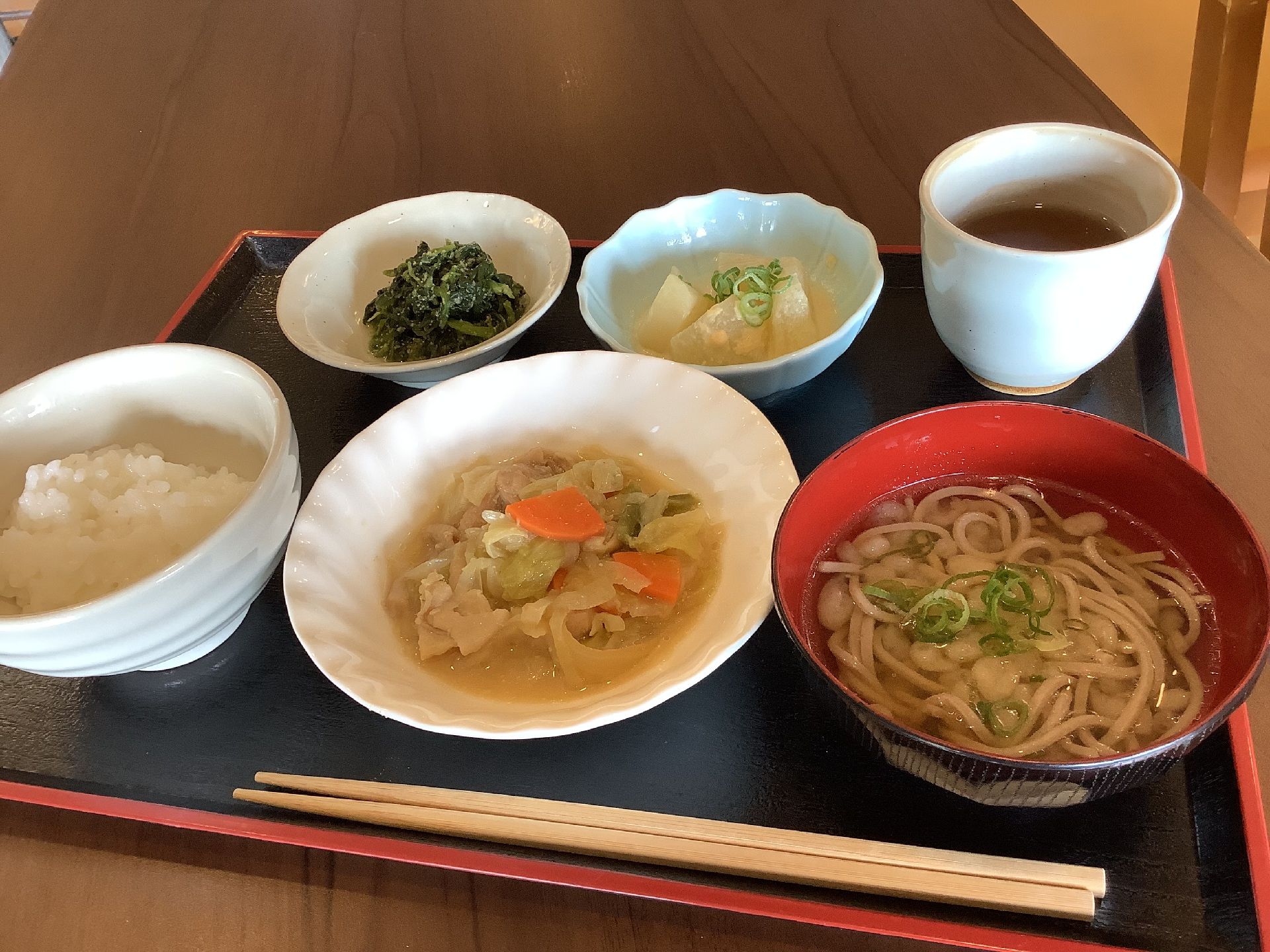 帽子をかぶった高齢女性が若い女性スタッフたちと一緒に花を見物しながら歩いている。