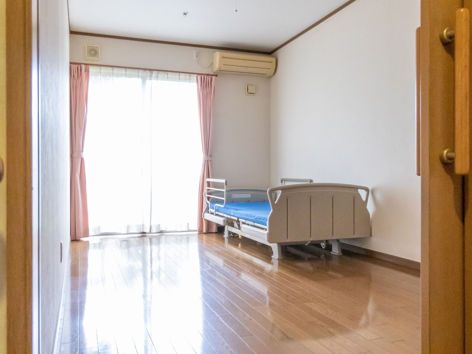 大きな窓から明るい自然光の入るベッドが設置された居室